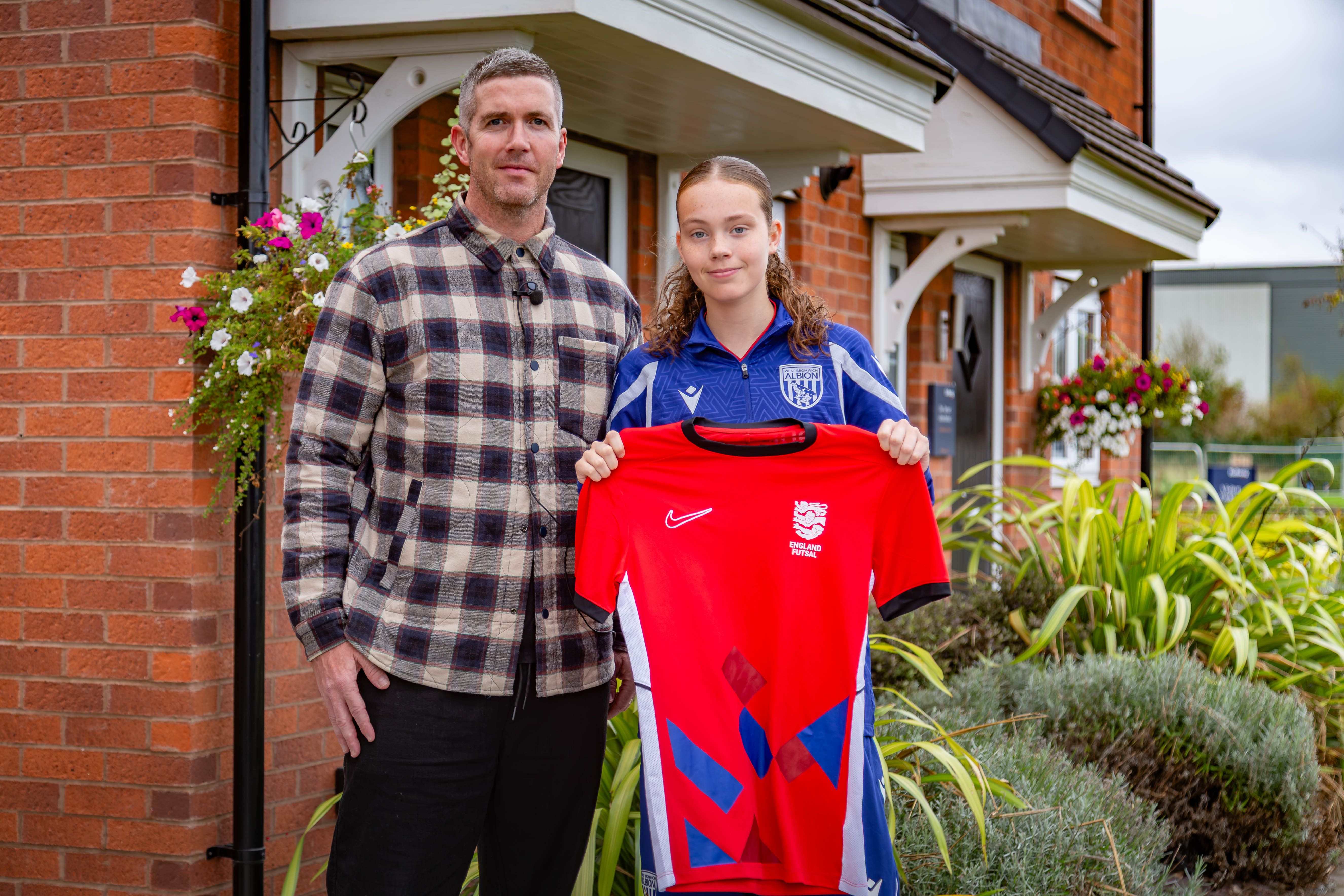 Two people holding an England futsal shirt outside homes at Sheasby Park